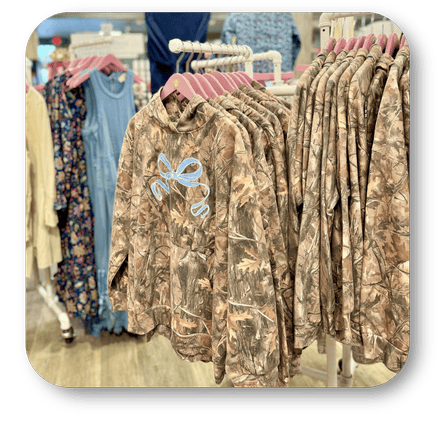 Camouflage hoodies with a blue bow design on hangers at Dewayne's in Selma, NC minutes from Raleigh, Cary, Clayton, Garner, Smithfield, Goldsboro