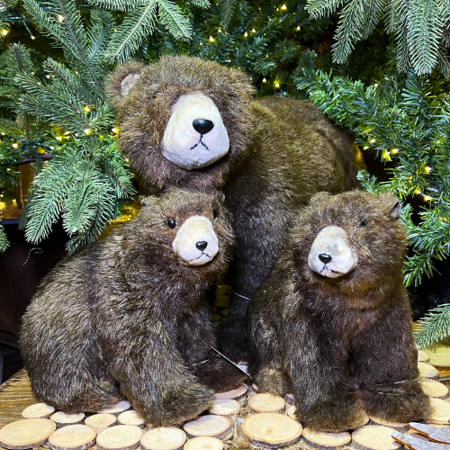 Three plush bears sitting together in front of a decorated Christmas tree.