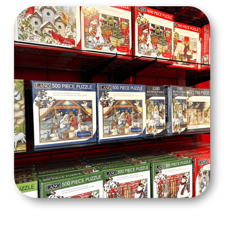 Display of LANG 500 piece puzzles on a shelf with various holiday-themed designs in the grand entrance room of christmas land 2025 at Dewayne's in Selma, NC minutes from Raleigh, Cary, Clayton, Garner, Smithfield, Goldsboro