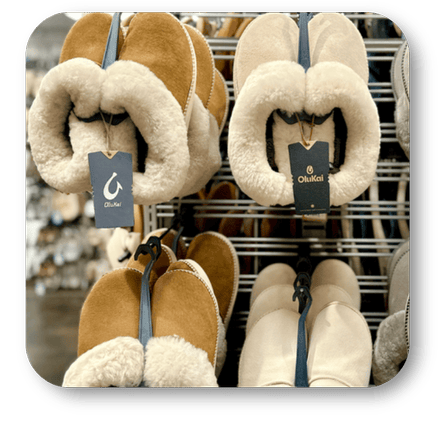 Pair of plush slippers with fluffy interior on a rack, featuring the Olukai brand at Dewayne's in Selma, NC minutes from Raleigh, Cary, Clayton, Garner, Smithfield, Goldsboro