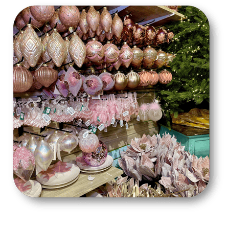 Decorative pink Christmas ornaments on a stand with a Christmas tree in the background in the gold and glamour room in christmas land 2025 at Dewayne's in Selma, NC minutes from Raleigh, Cary, Clayton, Garner, Smithfield, Goldsboro