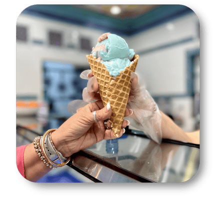 Hand holding a cone with blue ice cream in a blurred in the sweet shop at Dewayne's in Selma, NC minutes from Raleigh, Cary, Clayton, Garner, Smithfield, Goldsboro