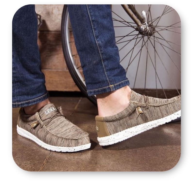 Brown casual Heydude shoes worn with jeans, standing on a wooden floor with a bicycle wheel in the background  in the men's shoppe at Dewayne's in Selma, NC minutes from Raleigh, Cary, Clayton, Garner, Smithfield, Goldsboro