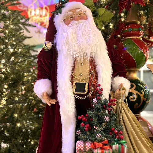 Decorative Santa Claus figure with a Christmas tree and gifts in front of a decorated Christmas tree.