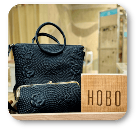 Black Hobo handbag with floral patterns on a wooden surface, with 'Hobo' branding visible in the boutique at Dewayne's in Selma, NC minutes from Raleigh, Cary, Clayton, Garner, Smithfield, Goldsboro