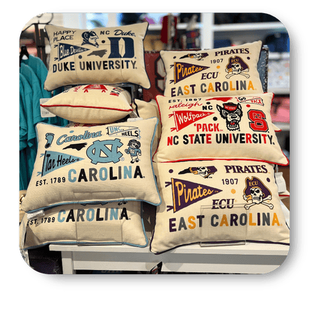 Collection of college-themed pillows with various university logos and designs at Dewayne's in Selma, NC minutes from Raleigh, Cary, Clayton, Garner, Smithfield, Goldsboro