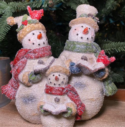 Decorative snowman family with a child, wearing scarves and hats, against a Christmas tree background in the country Christmas room of Christmas Land 2025 at Dewayne's