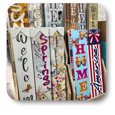 Decorative porch signs with 'Hello Spring' and 'Home' text, along with floral and patterned designs in the greenhouse atrium at Dewayne's in Selma, NC minutes from Raleigh, Cary, Clayton, Garner, Smithfield, Goldsboro 