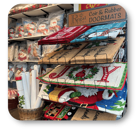 Display of various holiday doormats with Christmas designs on a shelf at Dewayne's in Selma, NC minutes from Raleigh, Cary, Clayton, Garner, Smithfield, Goldsboro