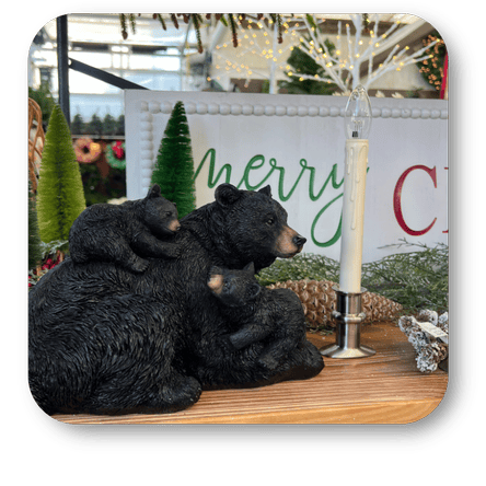 Two black bear figurines with a baby bear on a wooden surface, with a 'merry Christmas' sign in the background at Dewayne's in Selma, NC minutes from Raleigh, Cary, Clayton, Garner, Smithfield, Goldsboro