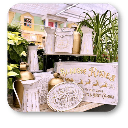 Decorative Christmas items including signs and watering cans in a greenhouse setting at Dewayne's in Selma, NC minutes from Raleigh, Cary, Clayton, Garner, Smithfield, Goldsboro