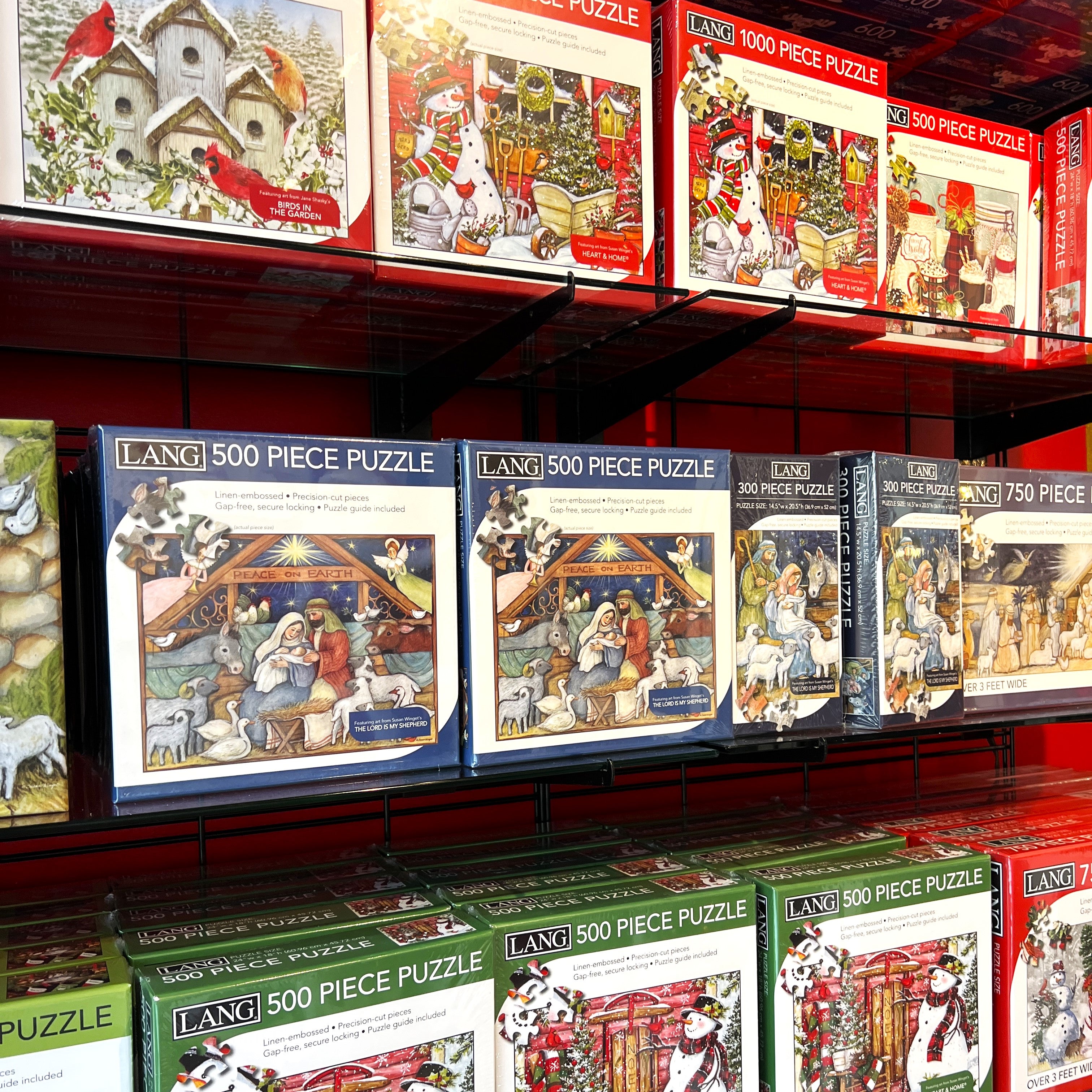 Display of LANG 500 piece puzzles on a shelf with various holiday-themed designs.