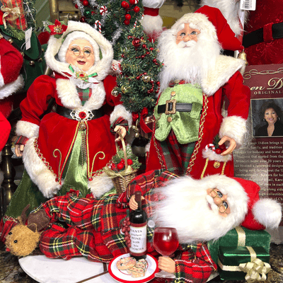 Decorative Christmas figures including Santa Claus and Mrs. Claus with a bottle of wine and food figurines by Karen Didion in the timeless treasures room in christmas land 2025 at Dewayne's