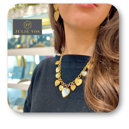 Woman wearing a Julie Vos gold necklace with heart-shaped pendants, blurred background with 'Julie Vos' branding  in the boutique at Dewayne's in Selma, NC minutes from Raleigh, Cary, Clayton, Garner, Smithfield, Goldsboro