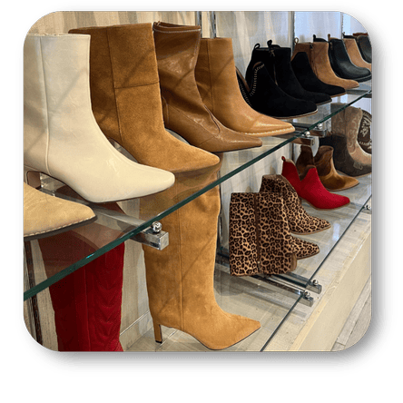 Display of various boots including beige, brown, black, and red on a glass shelf in the boutique at Dewayne's in Selma, NC minutes from Raleigh, Cary, Clayton, Garner, Smithfield, Goldsboro