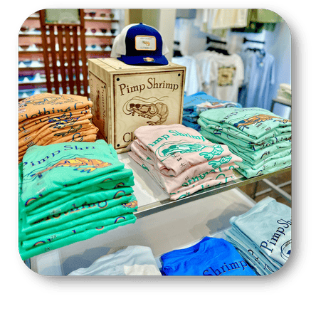 Stacks of t-shirts with 'Pimp Shrimp' branding on a table in the men's shoppe at Dewayne's in Selma, NC minutes from Raleigh, Cary, Clayton, Garner, Smithfield, Goldsboro