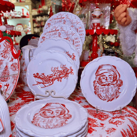 Set of Christmas-themed plates with Santa Claus designs on a table in the wrapped in red room in christmas land 2025 at Dewayne's in Selma, NC minutes from Raleigh, Cary, Clayton, Garner, Smithfield, Goldsboro