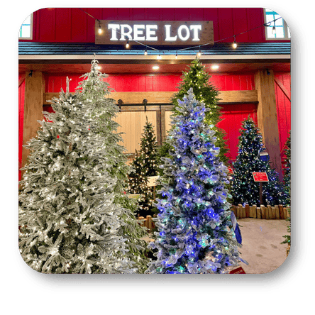 Decorated Christmas trees in a store with 'Tree Lot' sign above Display of candles and gift bags with a person in a Santa hat in a festive setting at Dewayne's in Selma, NC minutes from Raleigh, Cary, Clayton, Garner, Smithfield, Goldsboro